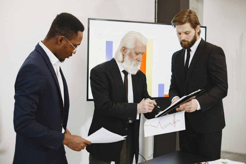 Three businessmen in suits reviewing reports and graphs during an office meeting.